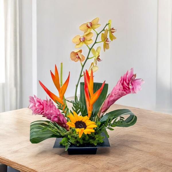Tropical floral arrangement with orchids, pink ginger, and a sunflower in a black vase