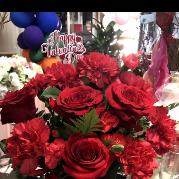 Red roses and carnations in a dark vase with a Valentine sign