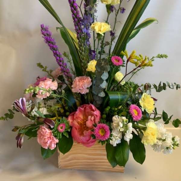 Mixed floral arrangement in a wooden box with tall purple spikes and pink blooms