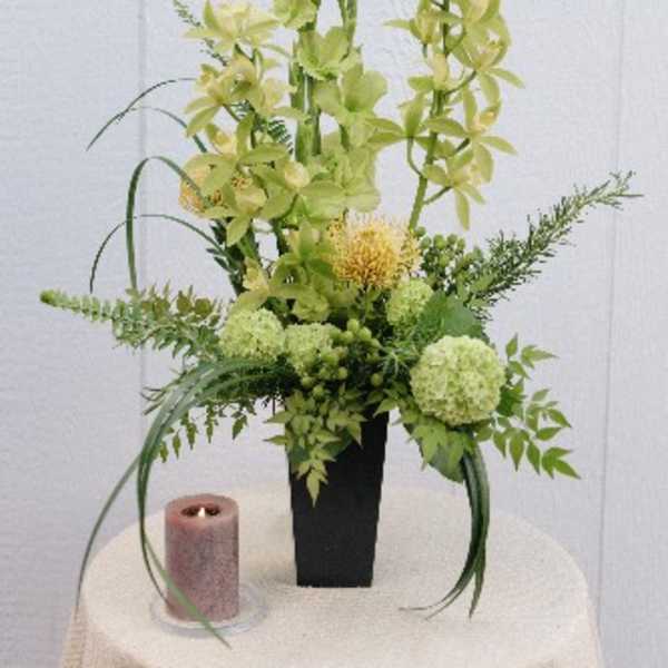 Tall green floral arrangement in a black vase with a pink candle beside it