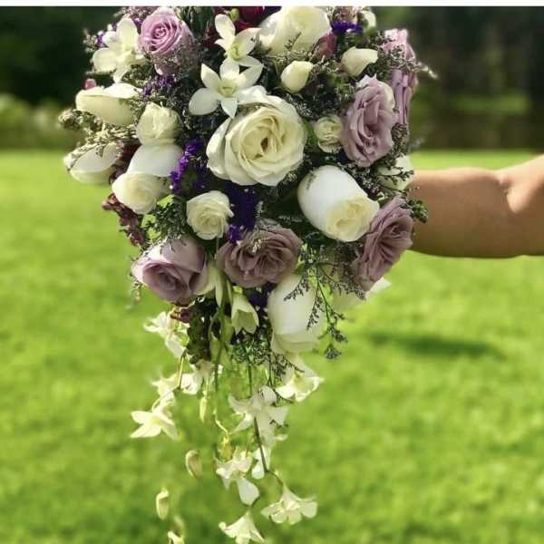 Handheld bouquet of white and lavender roses with trailing white orchids