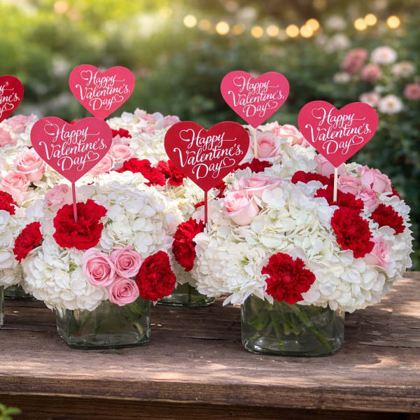 White and pink floral arrangements with red heart Valentine signs in glass vases