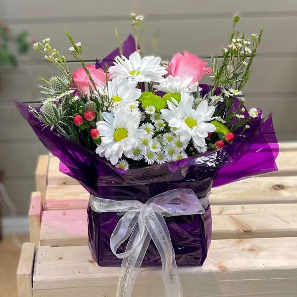 Bouquet of white daisies and pink roses wrapped in purple paper