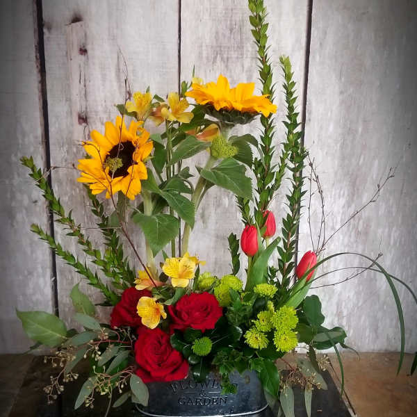 Mixed floral arrangement with sunflowers, red roses, and tulips in a black container
