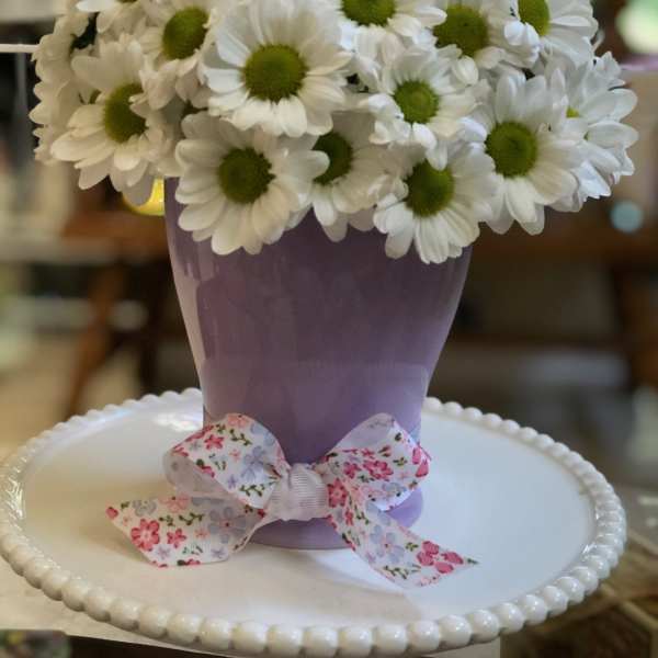 White daisies in a lavender vase with a floral ribbon bow