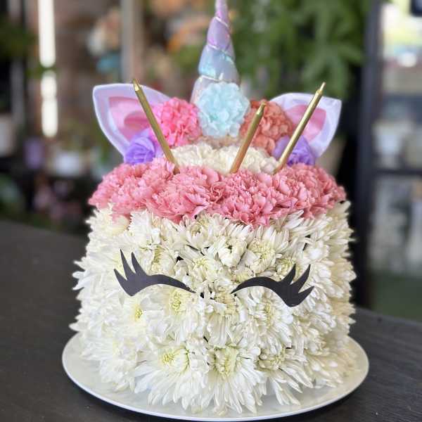 Unicorn-shaped floral cake with white and pink flowers on a round tray