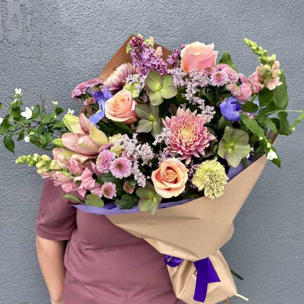 Large hand-tied bouquet of peach roses, pink lilies, and mixed blooms wrapped in kraft paper