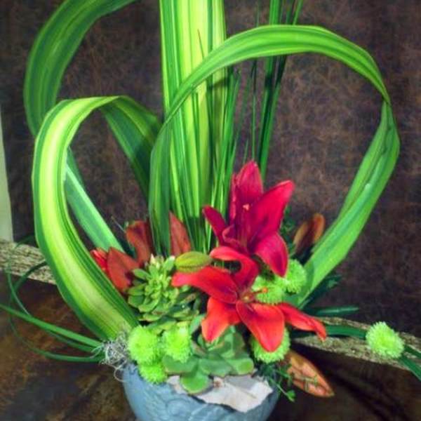 Modern floral arrangement with red lilies and green looped leaves in a blue bowl