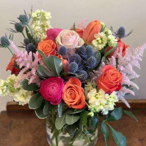Mixed bouquet of roses, tulips, and purple thistle in a glass vase