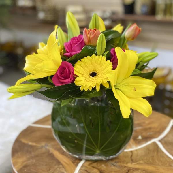 Yellow lilies, pink roses, and a yellow gerbera daisy in a glass vase