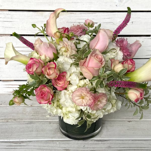 Low pink and white bouquet with roses, calla lilies, and hydrangeas in a glass cylinder vase