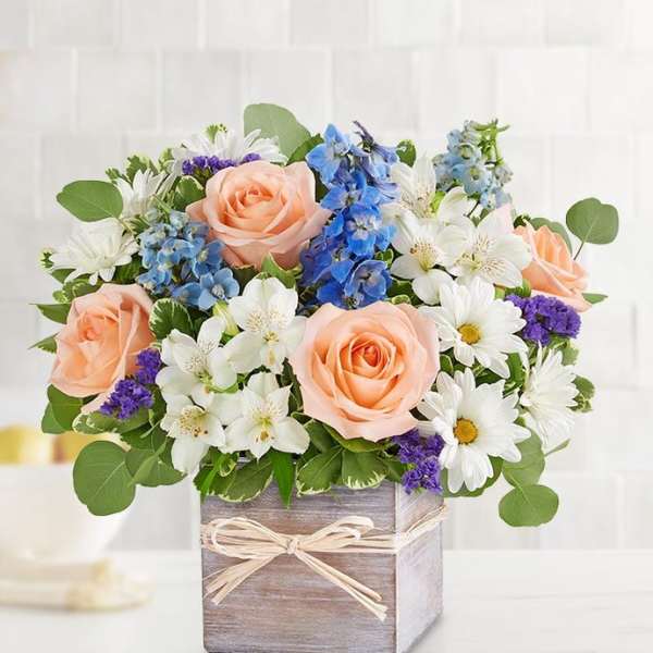Peach roses and white daisies in a wooden box with blue flowers