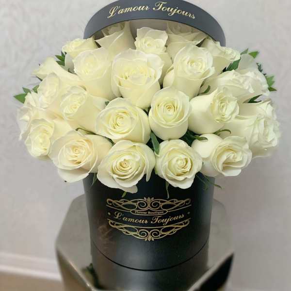 Round black hatbox filled with tightly packed ivory roses with gold script text.