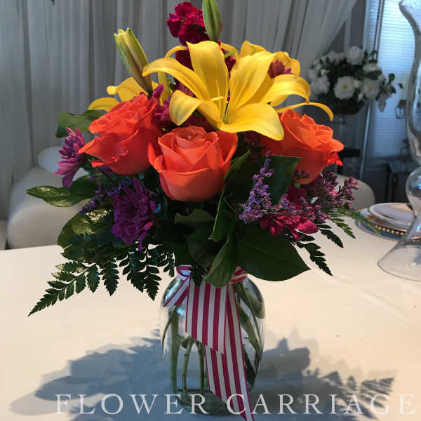 Bouquet of yellow lilies, orange roses, and purple flowers in a glass vase