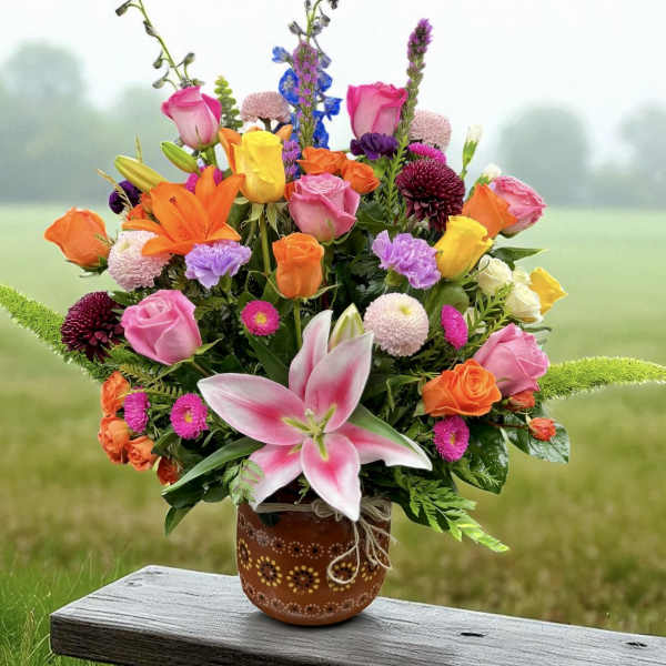 Colorful mixed bouquet of roses, lilies, and other blooms in a brown patterned ceramic pot.