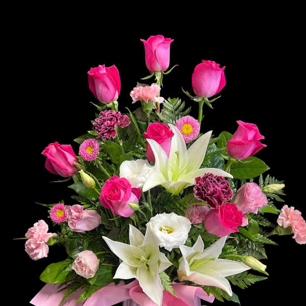 Pink and white arrangement with roses, lilies, and carnations in a pink vase with ribbon