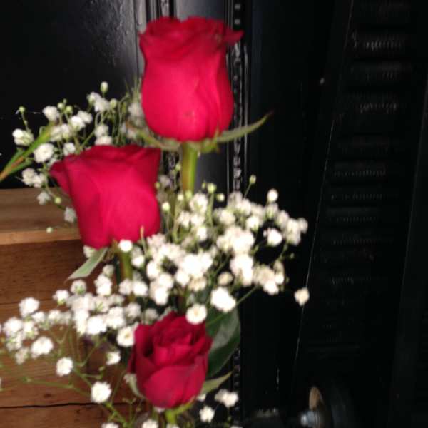 Three red roses with white baby's breath in a clear glass vase