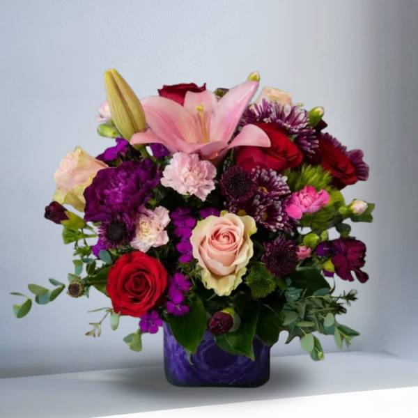 Mixed bouquet with pink lilies, red and blush roses in a purple vase