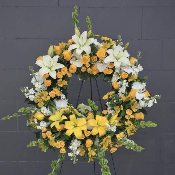 Circular floral wreath with white lilies, yellow roses, and white filler flowers