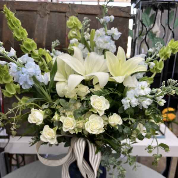 White lilies and roses in a dark vase with striped ribbon