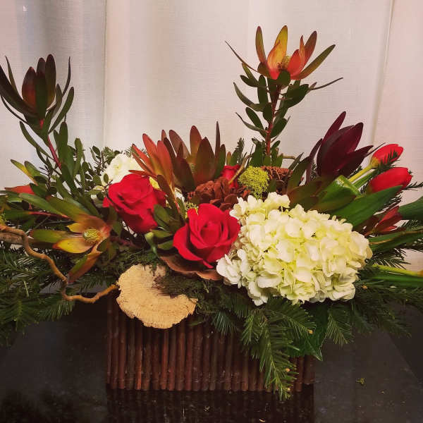 Low floral arrangement with red roses, white hydrangea, and tropical blooms in a rustic container