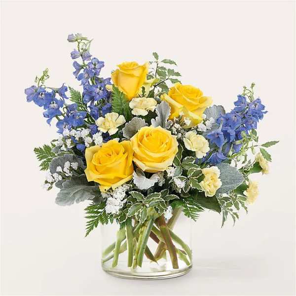 Yellow roses and blue delphinium in a clear glass vase