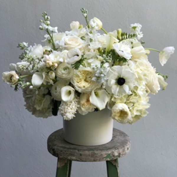 White floral arrangement in a cream vase on a stool