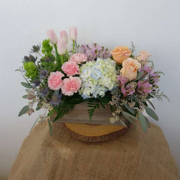 Mixed bouquet with pink tulips, roses, hydrangea, and carnations in a wooden box