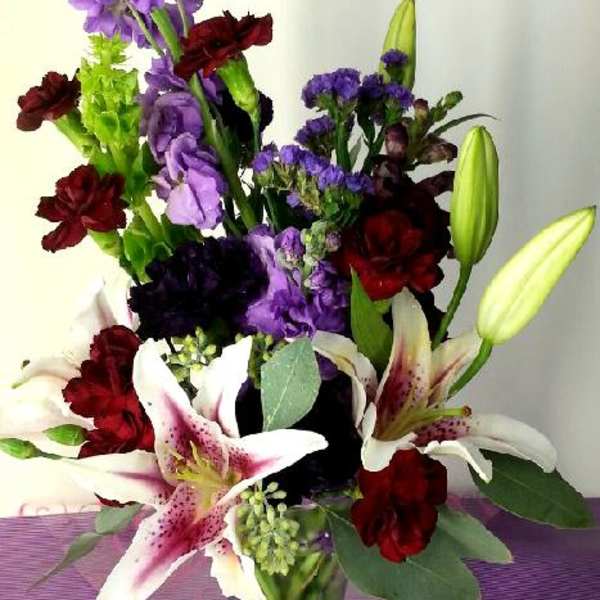 Mixed bouquet with lilies, purple blooms, and red carnations in a glass vase