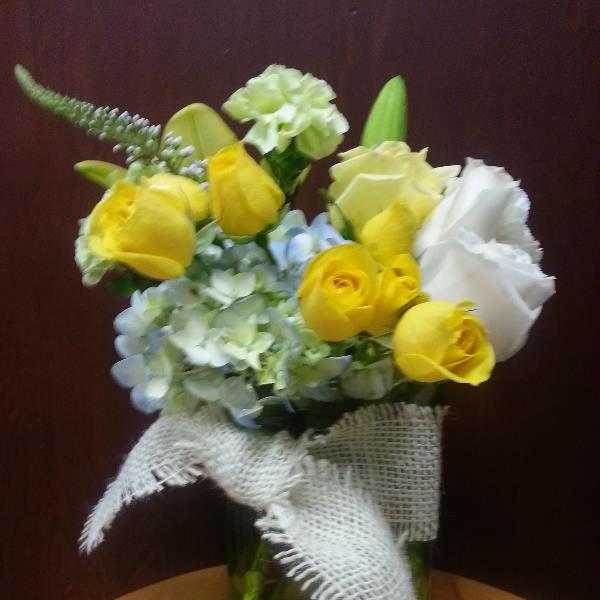 Yellow roses and pale blue hydrangeas in a glass vase with burlap ribbon