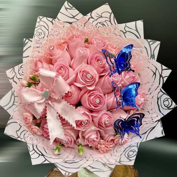 Round bouquet of pink roses with crystal centers, pink bow, and blue butterfly accents in patterned wrap
