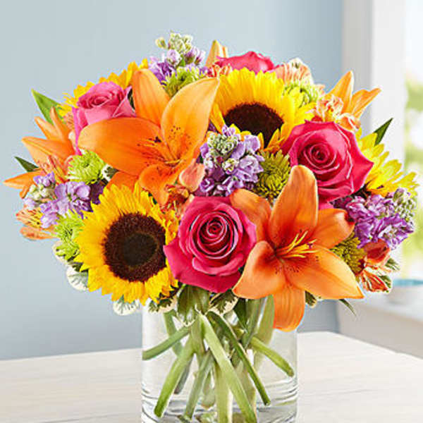 Bouquet of sunflowers, pink roses, and orange lilies in a glass vase