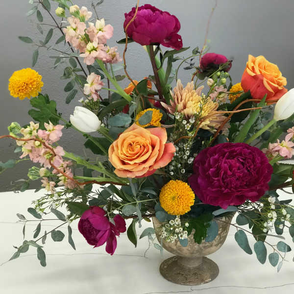 Mixed bouquet of roses, peonies, and tulips in a pedestal vase