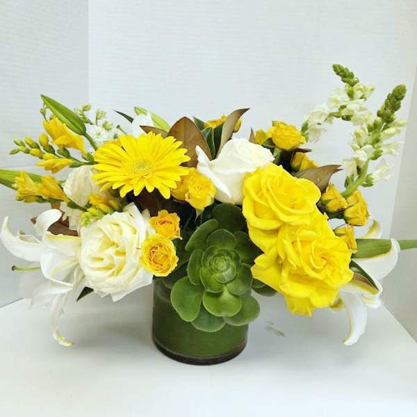Yellow and white floral arrangement in a green glass vase