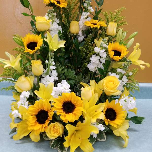 Yellow sunflowers, roses, and lilies arranged in a tall display