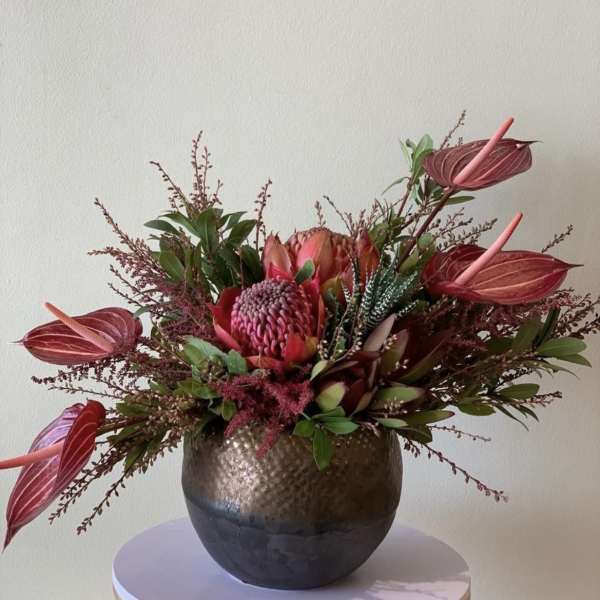Tropical floral arrangement in a round metallic vase with pink blooms