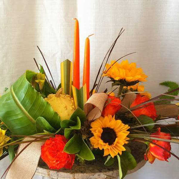 Orange and yellow floral arrangement with candles in a low container