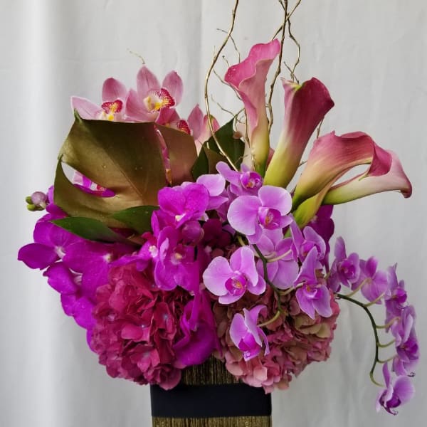 Pink orchids and calla lilies arranged in a tall gold vase