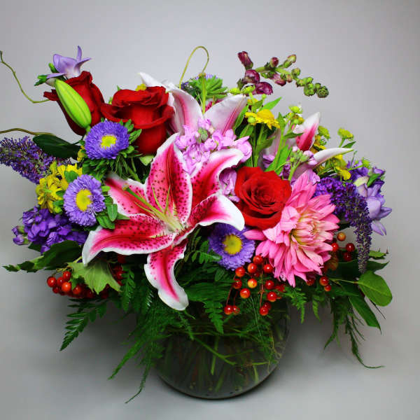 Colorful mixed bouquet with lilies, roses, and daisies in a glass vase