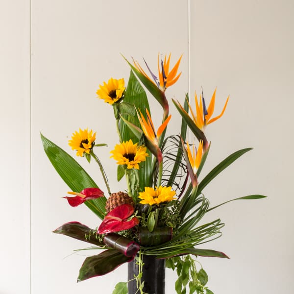 Tropical arrangement with sunflowers and bird of paradise in a black vase