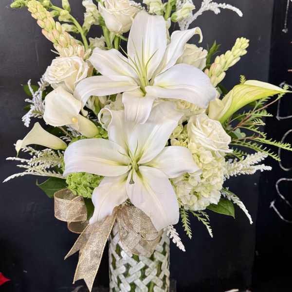 White lilies, roses, and calla lilies in a woven vase with a gold ribbon.