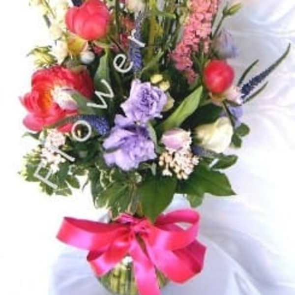 Tall mixed flower arrangement with a pink ribbon in a glass vase