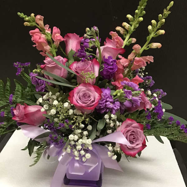 Pink and purple floral arrangement with roses and snapdragons in a ribbon-tied vase