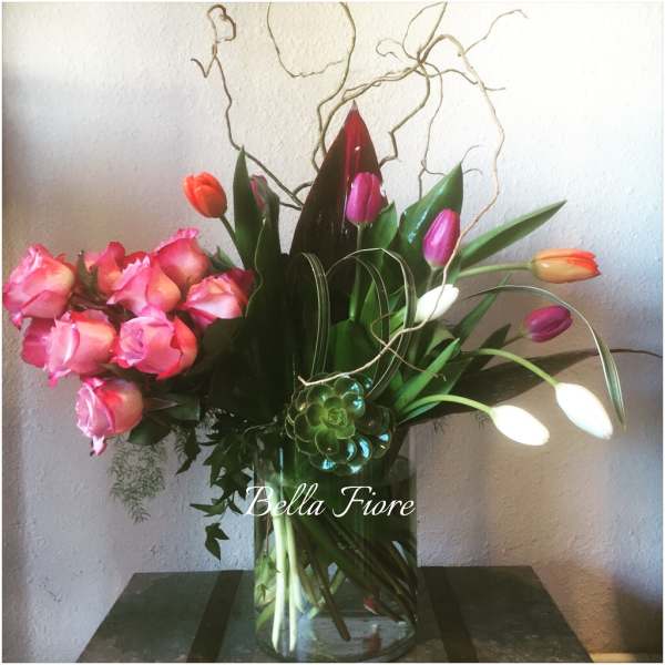Pink roses and colorful tulips arranged in a clear glass vase