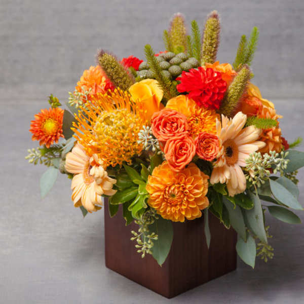 Orange and peach floral arrangement in a square wooden vase