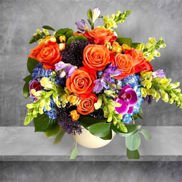 Colorful bouquet of orange roses, blue hydrangeas, and purple orchids in a white vase