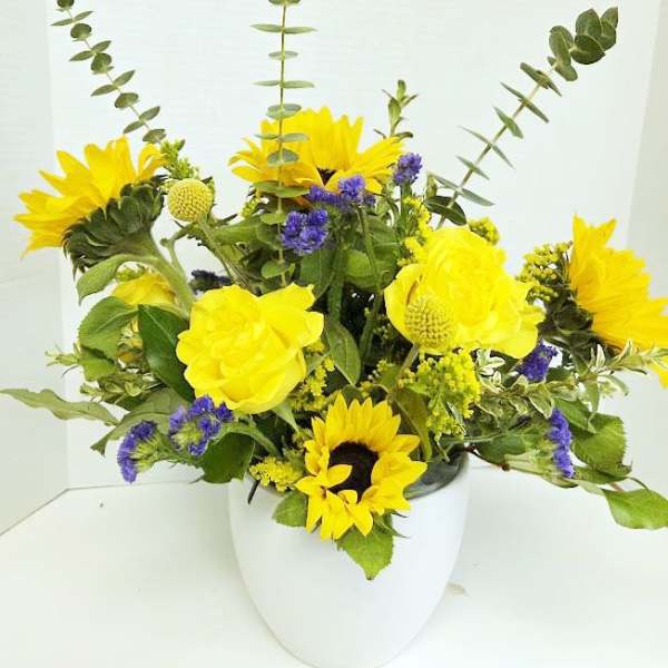 Yellow sunflowers and purple filler flowers in a white vase