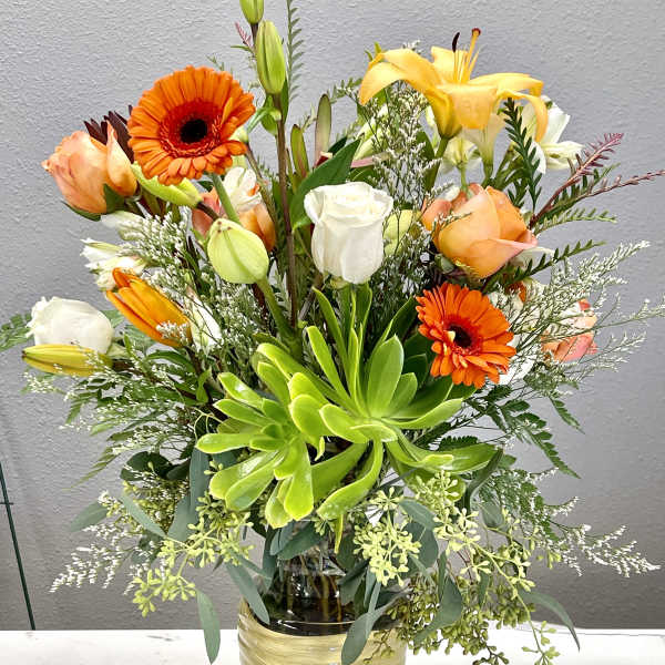Mixed bouquet with orange gerberas, lilies, and roses in a glass vase
