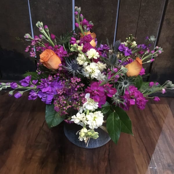 Mixed bouquet with orange roses, purple blooms, and white flowers in a low vase