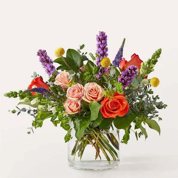 Mixed bouquet of roses and purple spikes in a clear glass vase